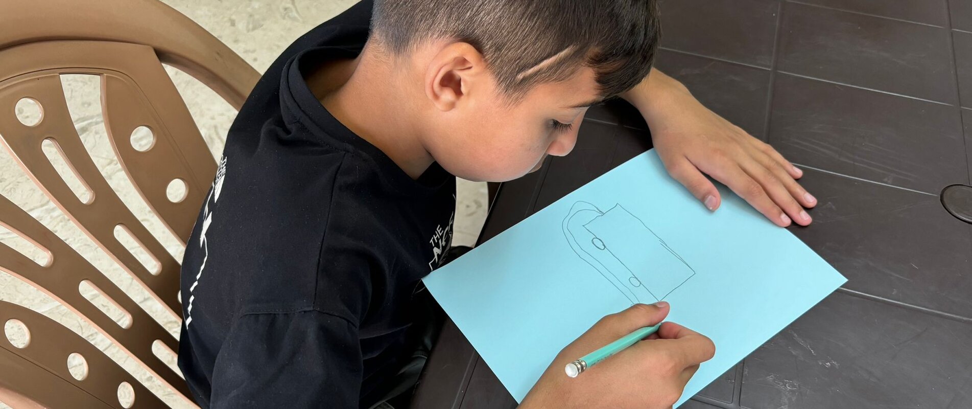 Kareem drawing a fire truck, sharing his dream of becoming a fireman. Three months ago, limited by his injury, he wished to be a carpenter. With nearly 90% recovery, his hopes have shifted back to firefighting, reflecting his progress and renewed sense of hope. Photo by © EJYMCA/Maha Sabbah